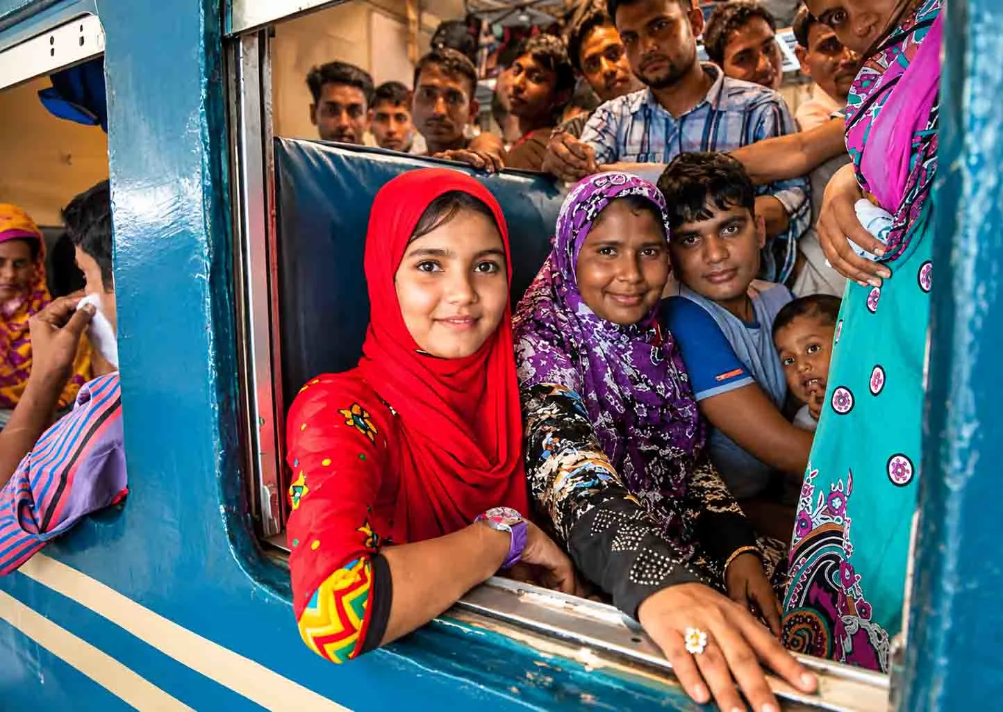 Passengers sharing a lively moment inside a local train in Bangladesh, looking through the open window during an everyday railway journey filled with community and cultural connections.