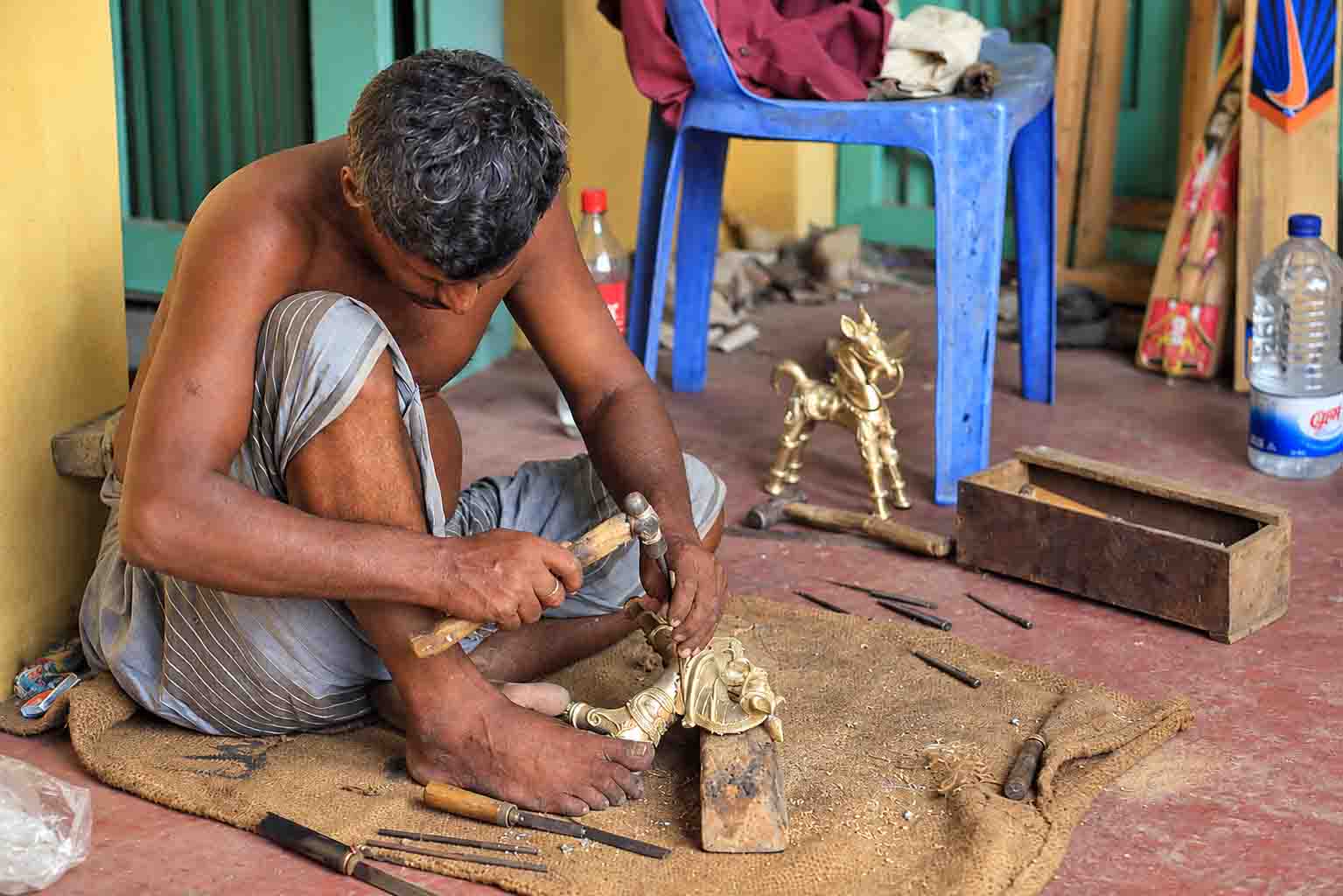A skilled artisan in Dhamrai, Bangladesh, handcrafting a decorative brass figure using traditional tools during the Brass & Pottery Tour.